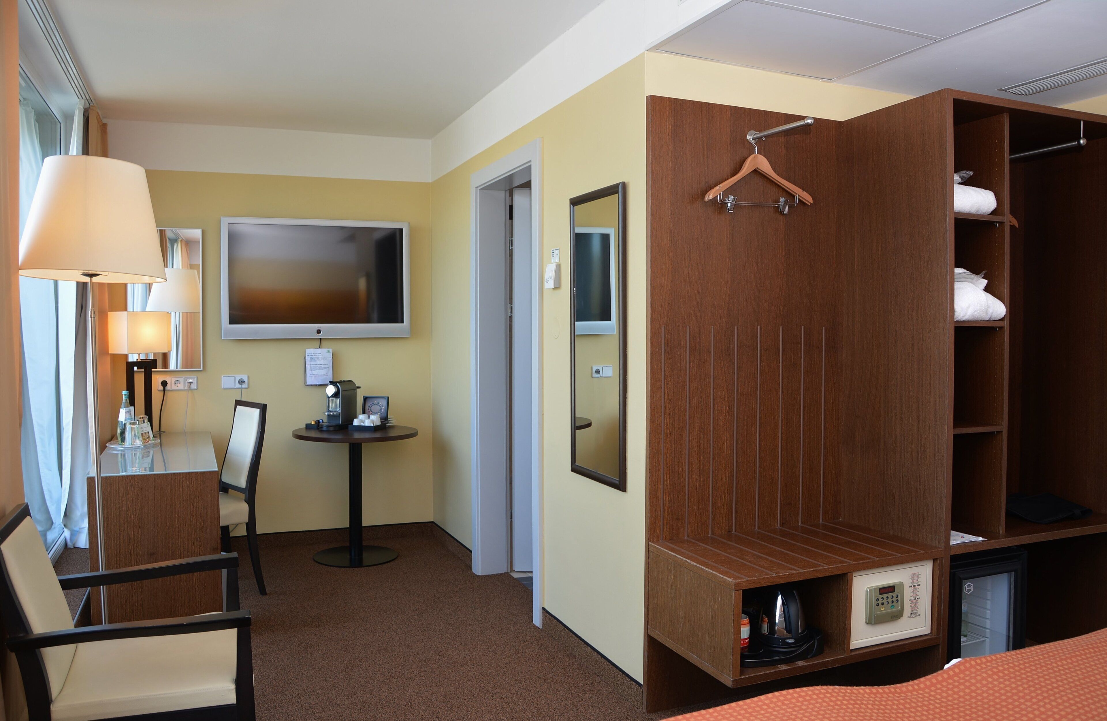 Une chambre d’hôtel avec une armoire en bois, un bureau avec une lampe, une télévision et une petite table sur laquelle se trouve une machine à café.
