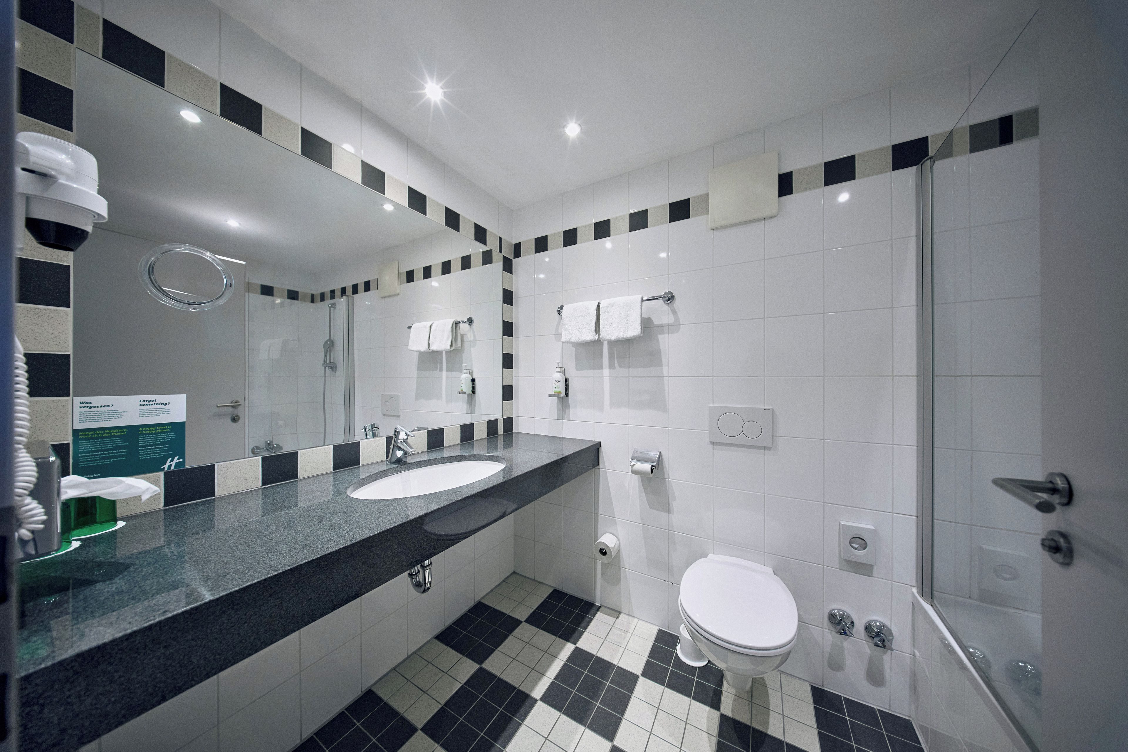 Une salle de bain moderne avec un sol à carreaux noirs et blancs, un grand miroir, un lavabo et des toilettes.