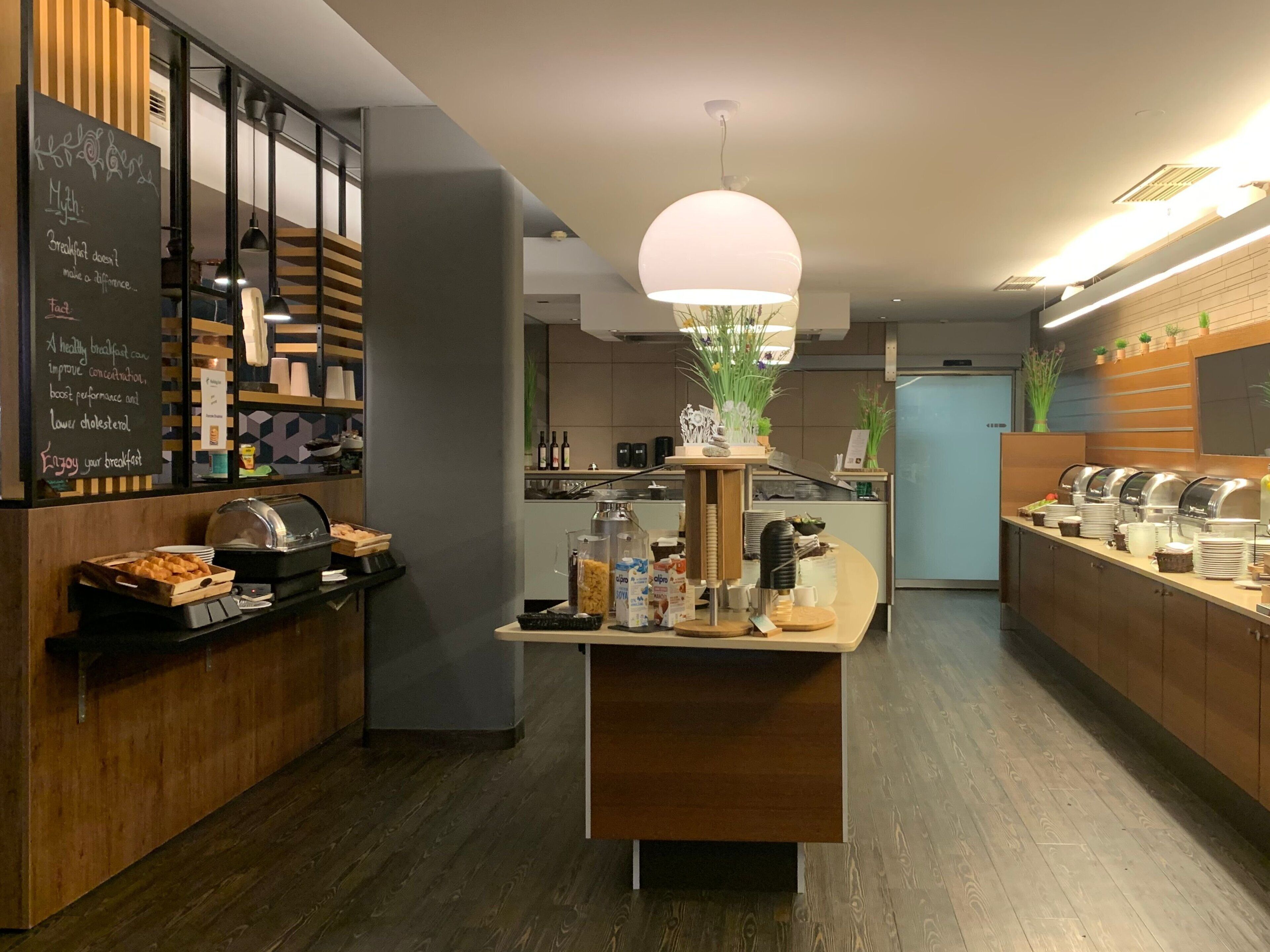 Un moderno comedor para desayunos con un menú en pizarra, una barra de buffet y una isla central con lámpara colgante.
