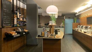 Un moderno comedor para desayunos con un menú en pizarra, una barra de buffet y una isla central con lámpara colgante.
