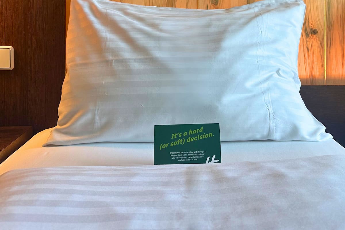 A neatly made bed with a pillow and a green sign on it.