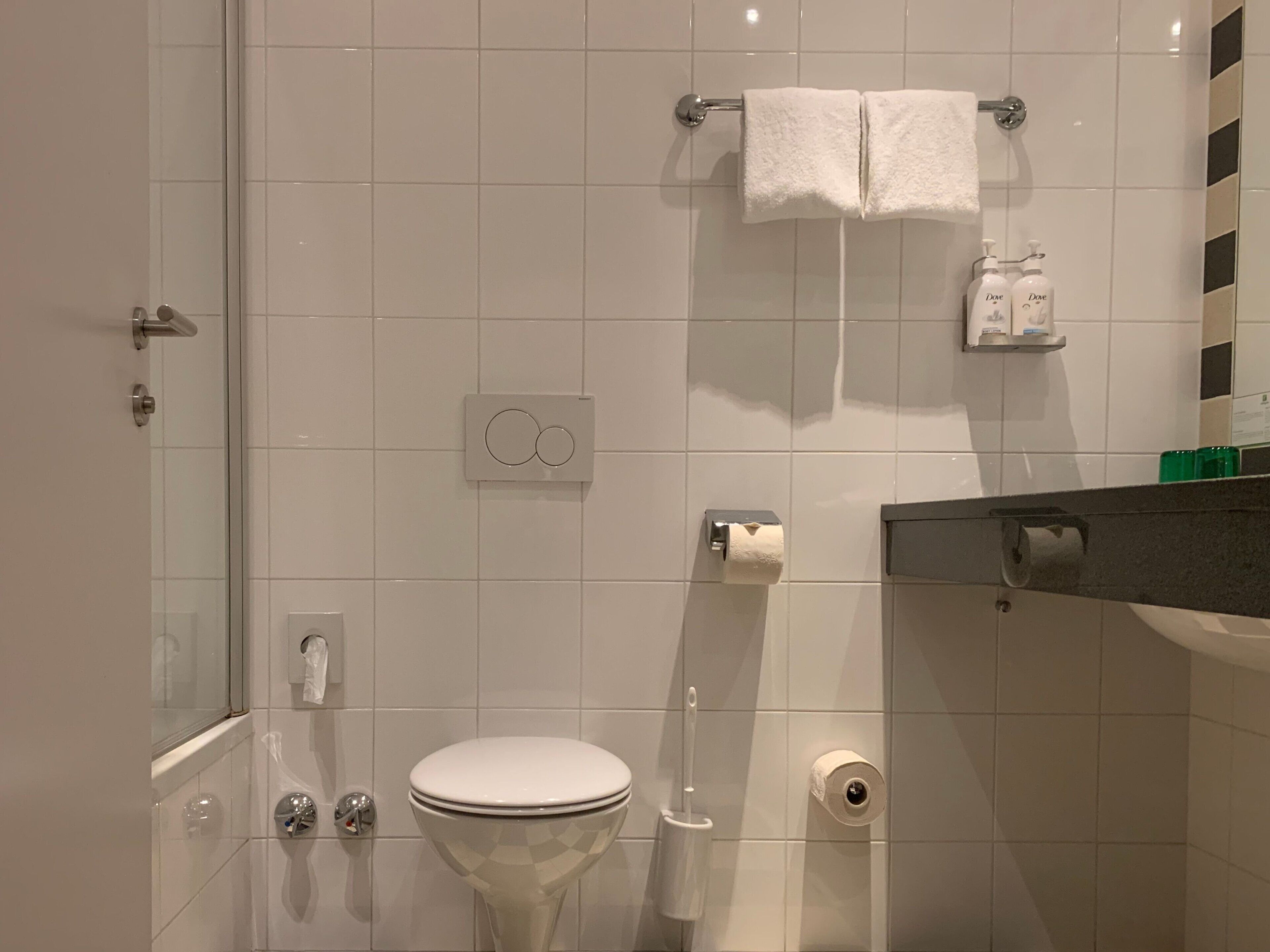 A modern bathroom with a toilet, bidet, and hand dryer. There are two white towels hanging on a towel rack.