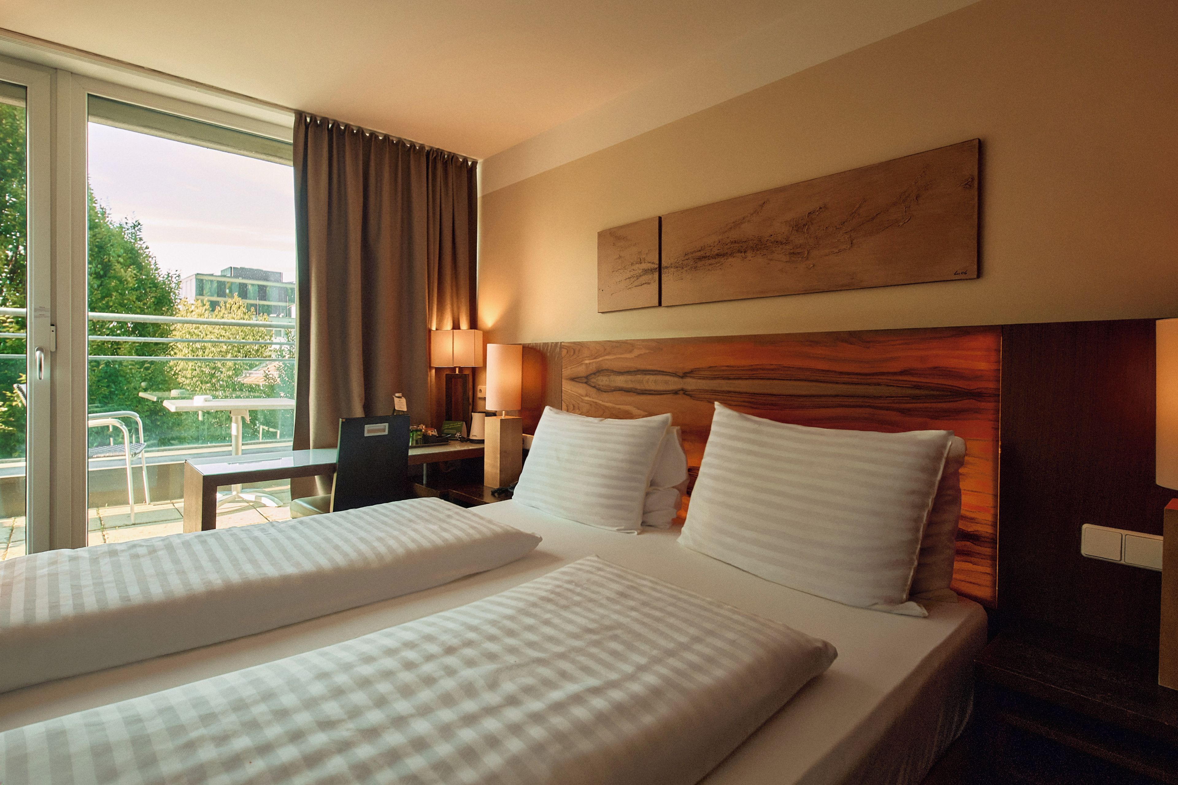 A hotel room with two beds, a desk, a chair, a lamp, and a painting on the wall.