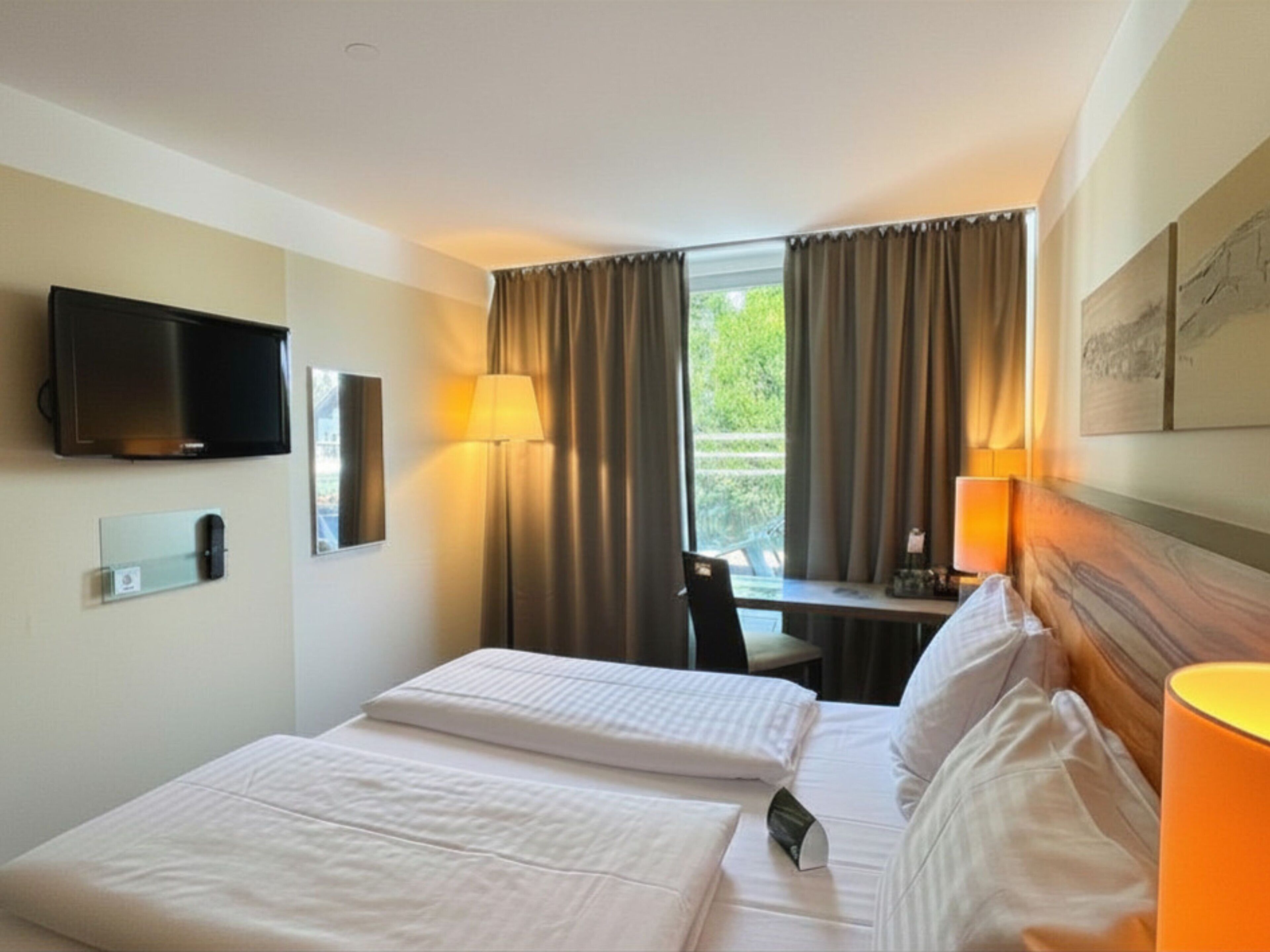 Une chambre d’hôtel avec deux lits, un bureau, une chaise, une télévision et une fenêtre avec des rideaux.