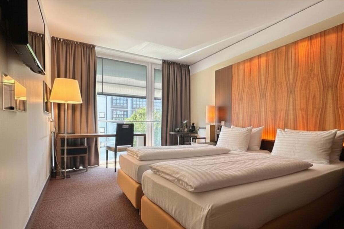 A hotel room with two beds, a desk, a chair, and a large window.