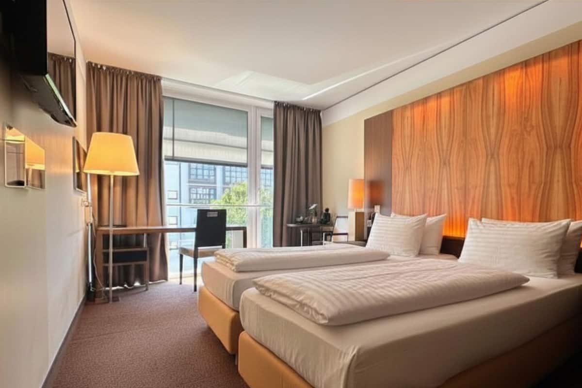Ein Hotelzimmer mit zwei Betten, einem Schreibtisch, einem Sessel und einem großen Fenster.