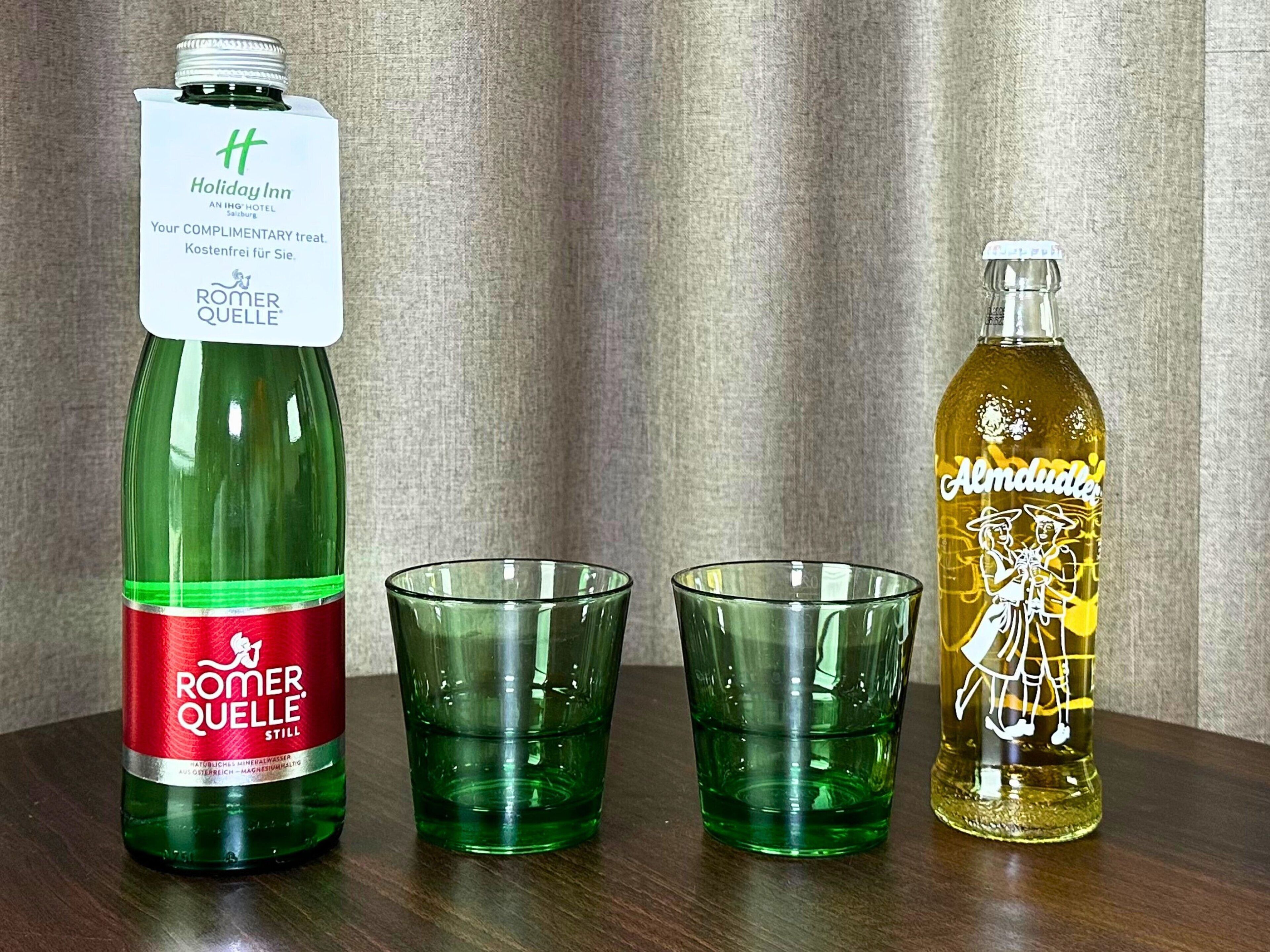 A bottle of Romer Quelle Still and a bottle of Almudale with two empty glasses on a wooden surface.