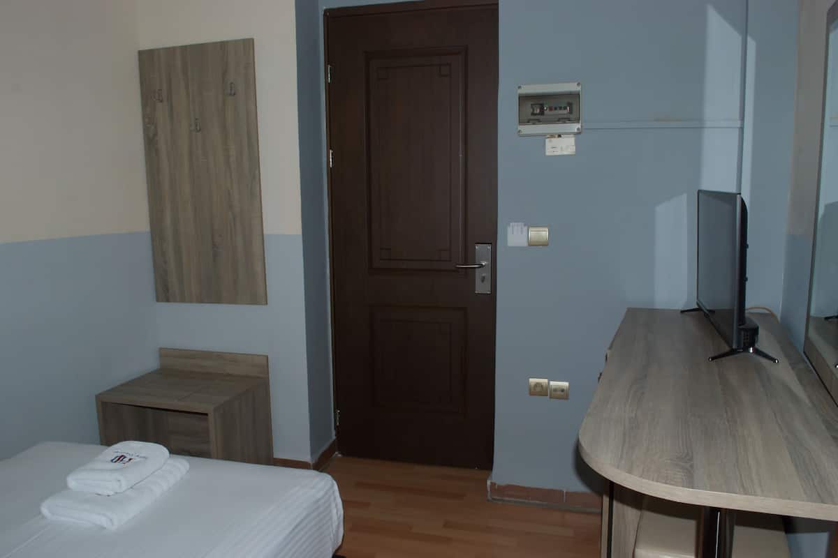 A hotel room with a bed, a wooden nightstand, a television, and a door.