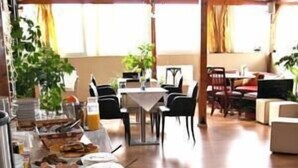 A dining area with a table set for four, surrounded by chairs. There are plants and a window in the background. - Hotel Diethnes (Athens)
