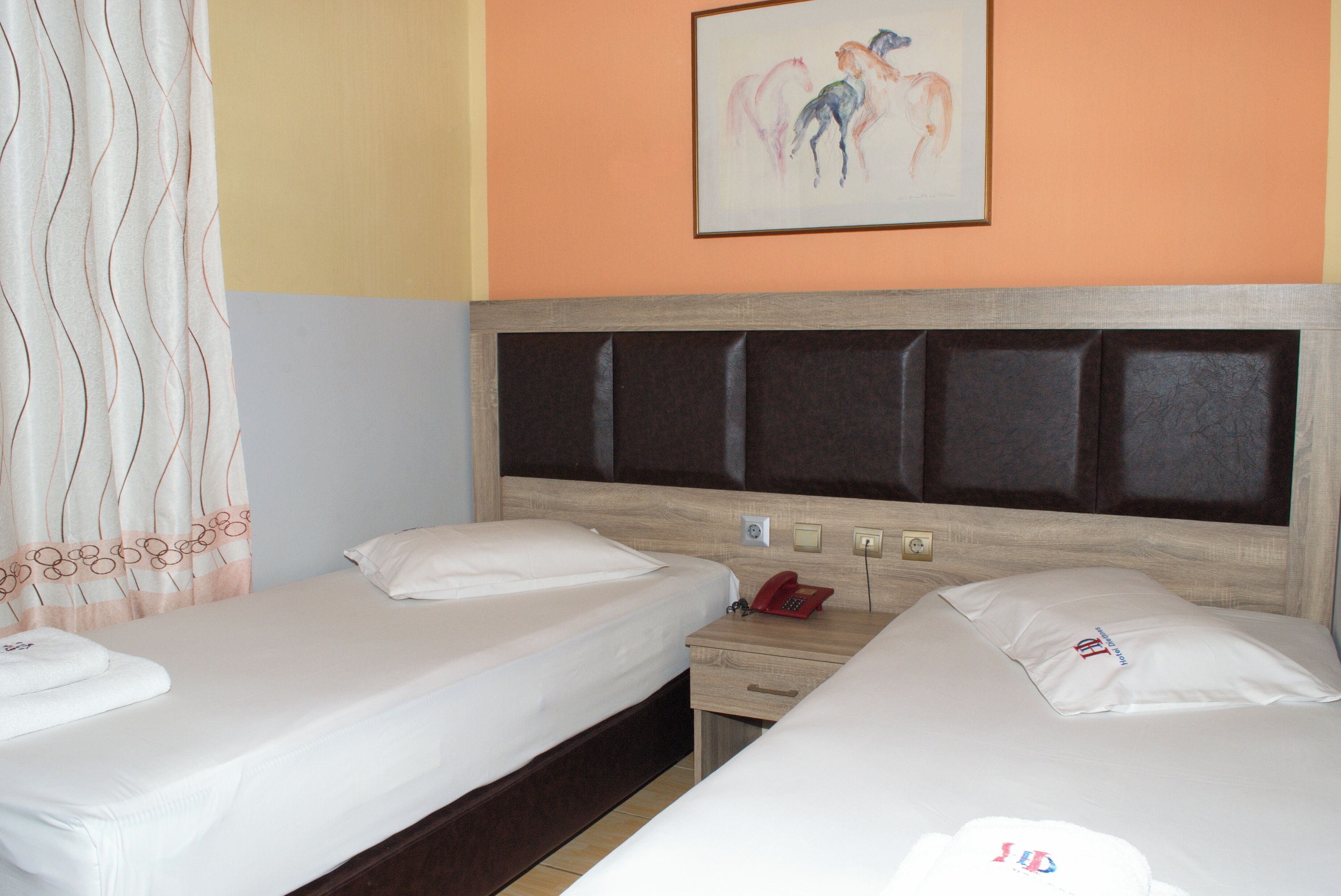Une chambre d’hôtel avec deux lits, une tête de lit en bois, une table de chevet avec un téléphone et un tableau au mur.