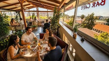 Ein Essbereich im Freien mit Tischen und Stühlen, Blick auf die Stadt und ein Restaurantschild.