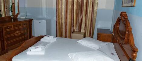 Ein ordentlich bezogenes Bett mit weißen Laken und Handtüchern, ein Holzschrank, ein kleiner Schreibtisch mit Telefon sowie ein an der Wand befestigter Fernseher.