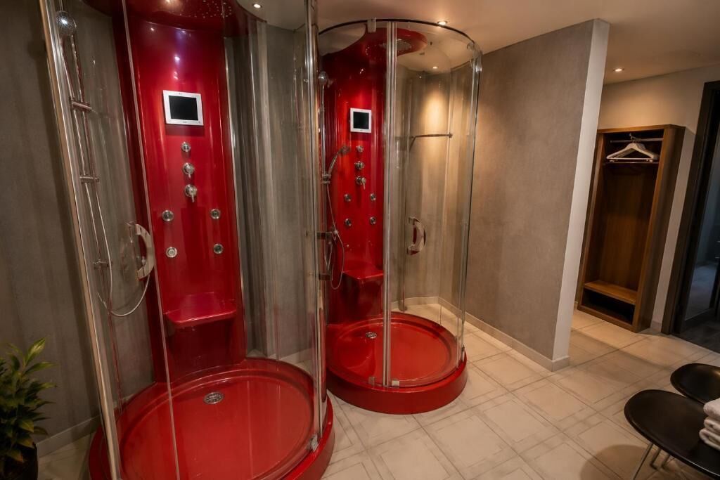 Ein modernes Badezimmer mit zwei roten, gläsernen Duschkabinen, einem Holzschrank und einem gefliesten Boden.