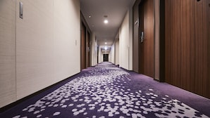 A hotel corridor with a purple carpet, wooden doors, and a light-colored wall. - JR East Hotel Mets Musashisakai (Musashino)