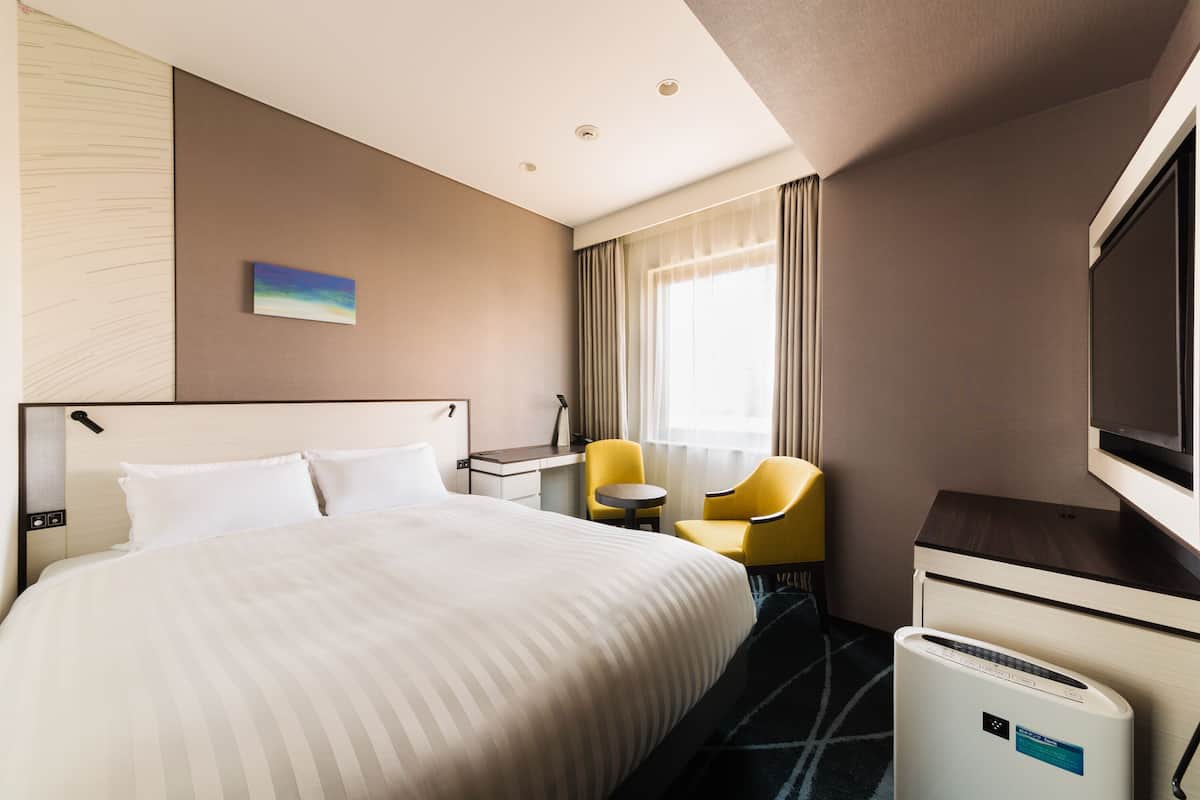 Une chambre d’hôtel équipée d’un lit, d’un bureau, d’une chaise, d’une télévision et d’un mini-bar.