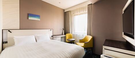 A hotel room with a bed, a desk, a chair, a TV, and a minibar.