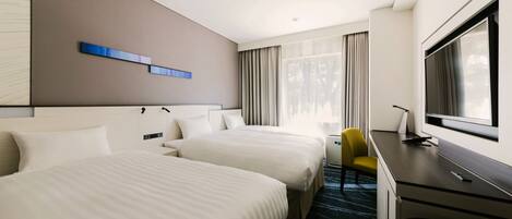 A hotel room with two beds, a desk, a chair, a TV, and a window with curtains.