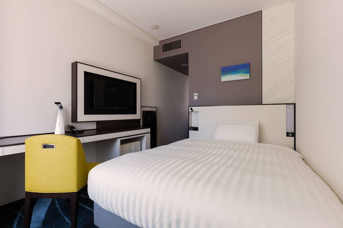 Une chambre d’hôtel avec un lit, un bureau doté d’un téléviseur à écran plat, une chaise et un tableau au mur.