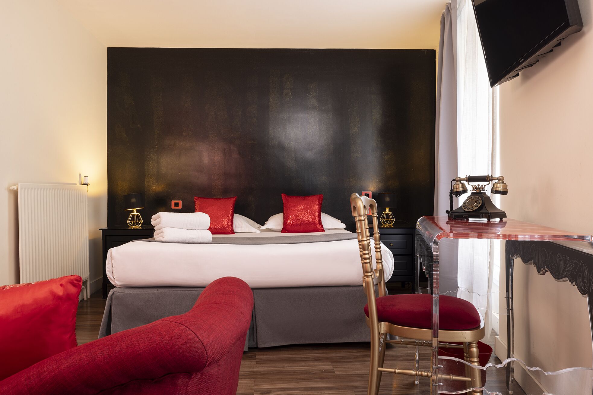 Une chambre d’hôtel avec un lit, un bureau avec un téléphone et une chaise rouge.