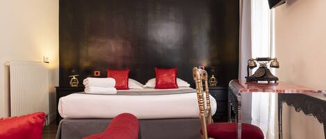 Une chambre d’hôtel avec un lit, un bureau avec un téléphone et une chaise rouge.