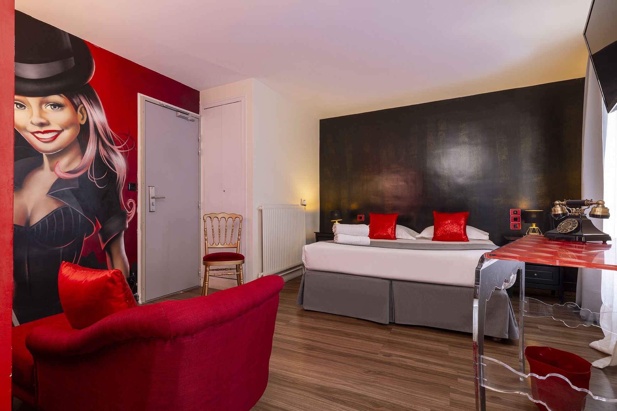 A modern hotel room with a large bed, a red chair, a vintage telephone, and a red and black wall mural.