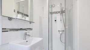 A modern bathroom with a white sink, a glass shower enclosure, and a tiled backsplash. - Hôtel Paris Legendre (Paris)