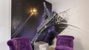 A room with two purple upholstered chairs, a metallic suitcase, and a wall mural of the Eiffel Tower. - Hôtel Paris Legendre (Paris)