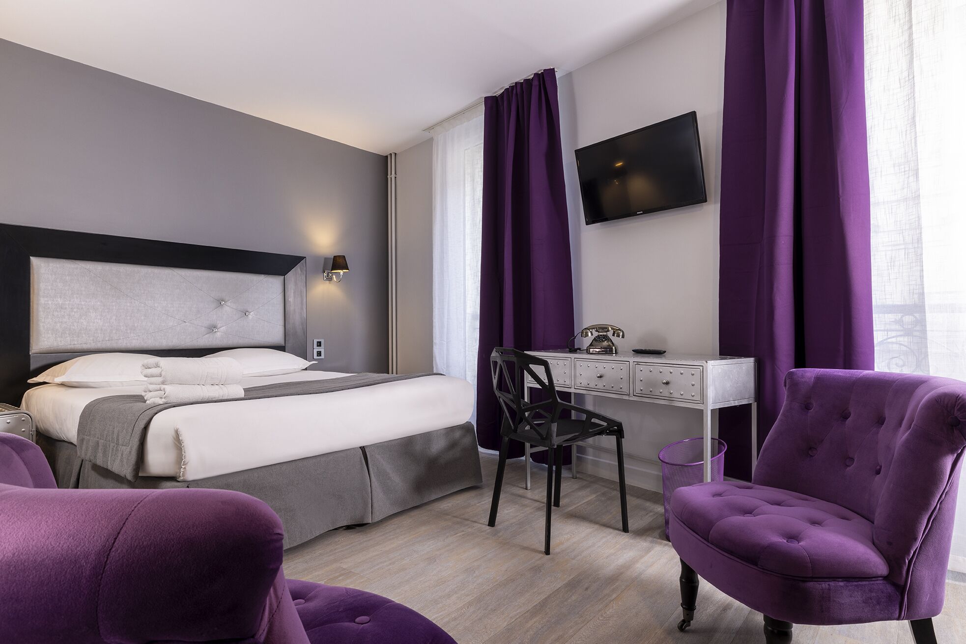 Ett modernt hotellrum med en säng, ett skrivbord, en stol och en TV.