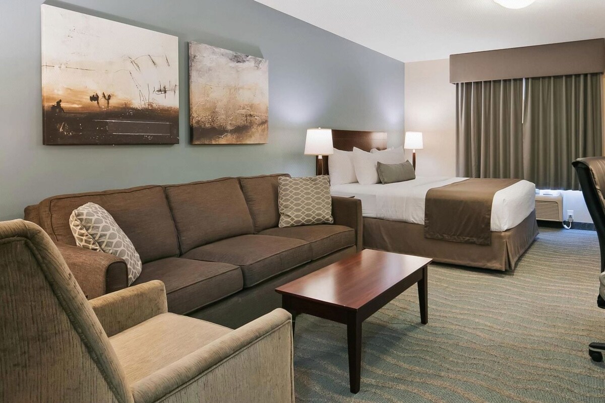 Ein Hotelzimmer mit einer Couch, einem Bett, einem Sessel, einem Couchtisch und zwei Wandlampen.