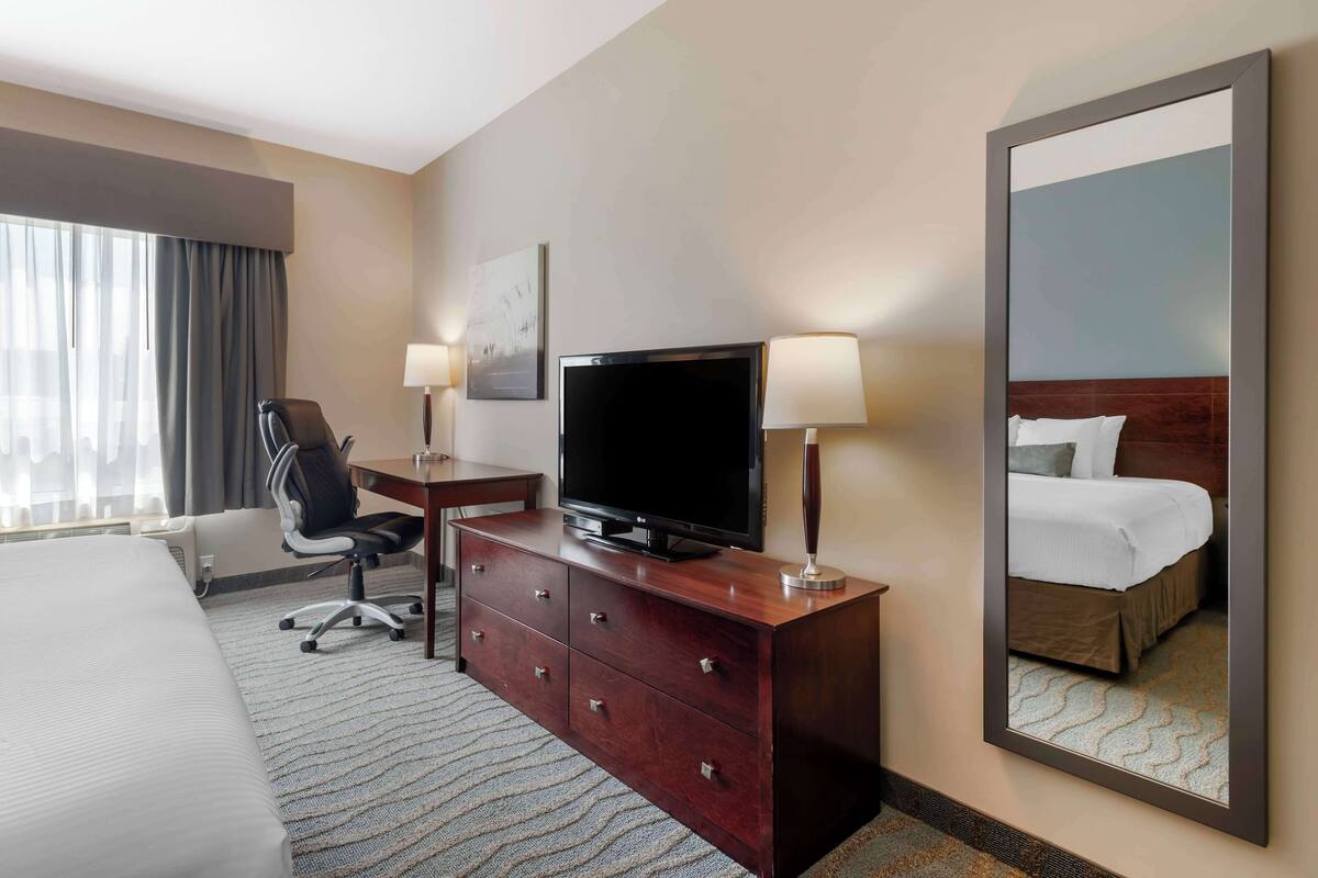 Une chambre d’hôtel comprenant un lit, un bureau avec une télévision, une chaise, une commode et un grand miroir.