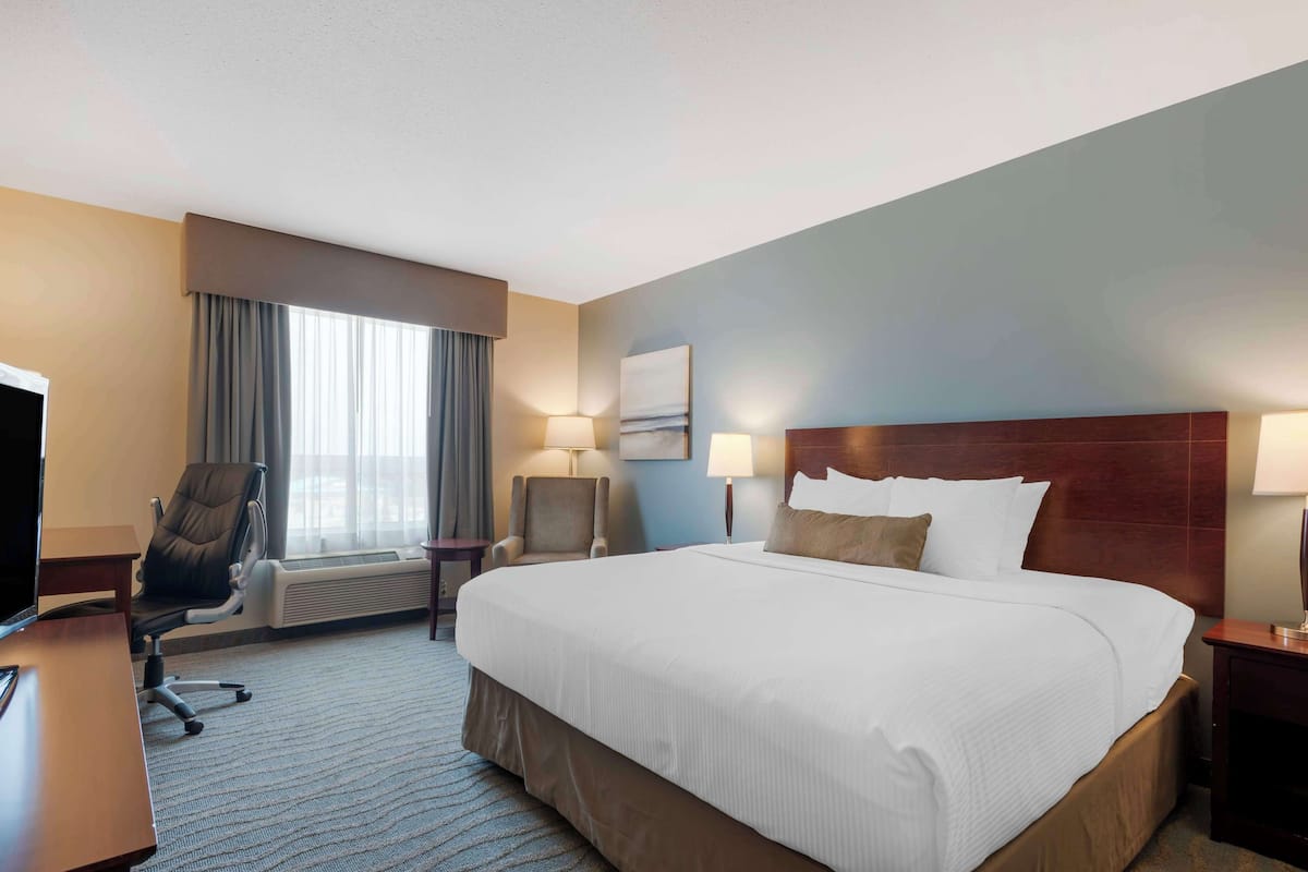 Une chambre d’hôtel avec un grand lit, un bureau avec une chaise, une télévision et une fenêtre avec des rideaux.