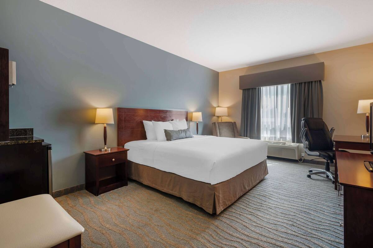 Une chambre d’hôtel avec un grand lit, deux tables de chevet avec des lampes, un bureau et une chaise.