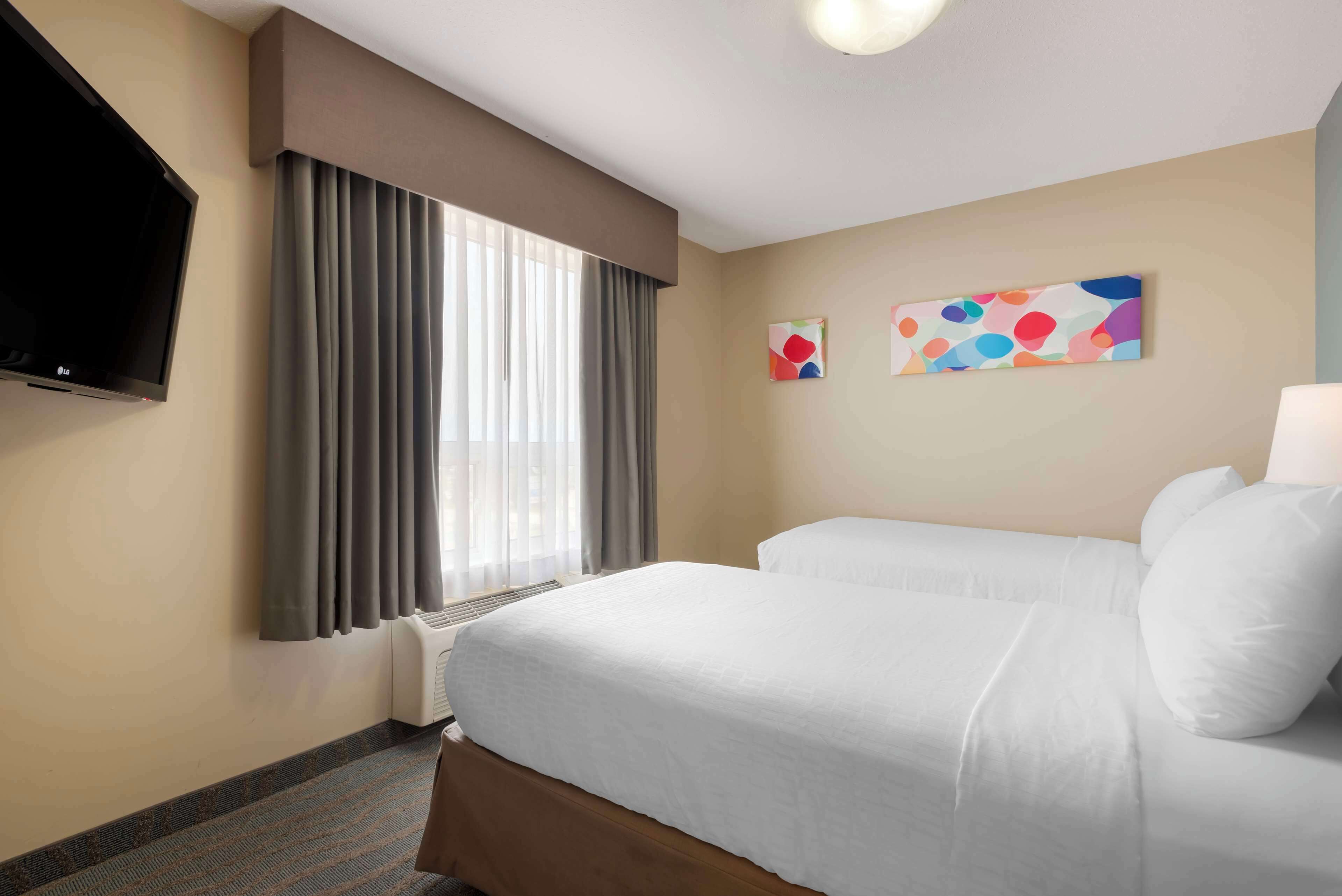 Habitación de hotel con una cama, un televisor, un ventanal con cortinas y dos obras de arte en la pared.