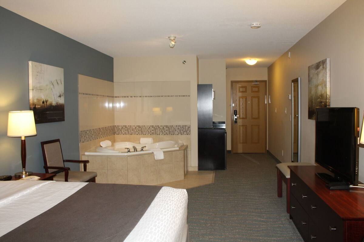 Une chambre d’hôtel comprenant un lit, un bureau, une télévision, une salle de bain avec baignoire et une porte donnant sur une autre pièce.