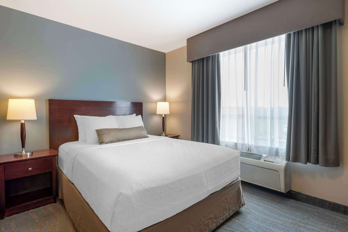 Une chambre d’hôtel avec un grand lit, deux tables de chevet avec des lampes, une fenêtre avec des rideaux et un appareil de climatisation.