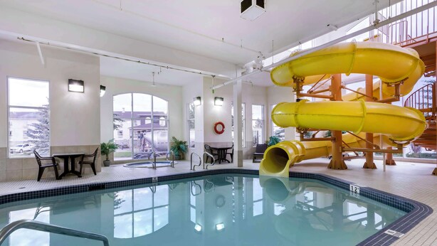 An indoor swimming pool with a slide, seating area, and large windows. - Best Western Rocky Mountain House Inn & Suites (Rocky Mountain House)