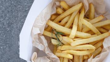 Un contenitore di patatine fritte con un rametto di rosmarino sopra, su una superficie strutturata.