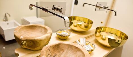 A bathroom with three wooden bowls as sinks, a white pedestal sink, and a mirror with a wooden frame.