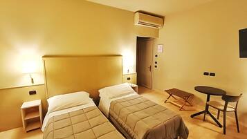 Ein Hotelzimmer mit zwei Betten, einem kleinen Tisch, einem Stuhl, einer Klimaanlage, einer Nachttischlampe und einer Tür.