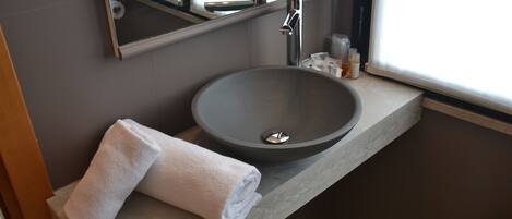 Un baño moderno con un lavamanos grande y de color oscuro, una toalla sobre la encimera y un ventanal que proporciona luz natural.