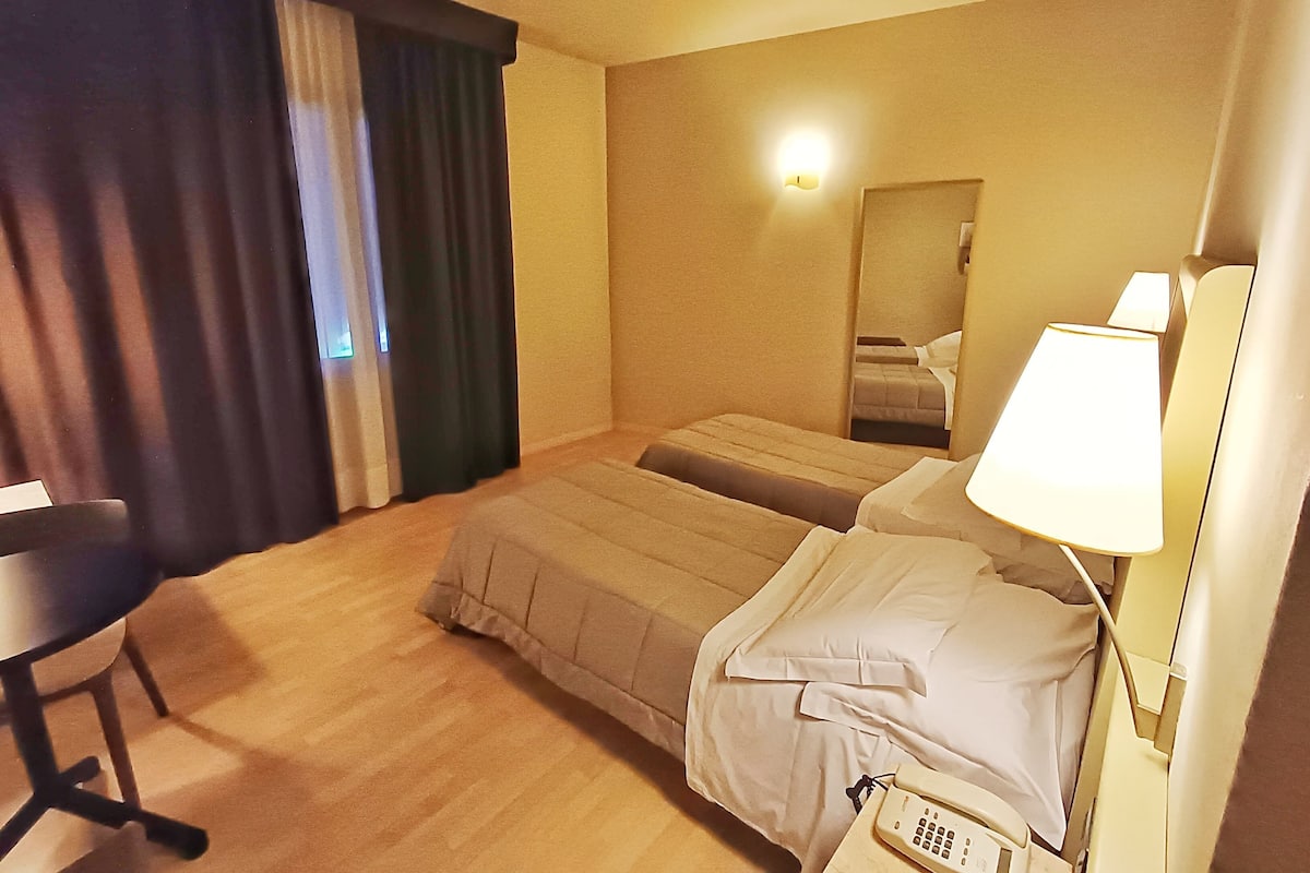 A hotel room with a bed, a desk, a chair, a lamp, and a telephone.