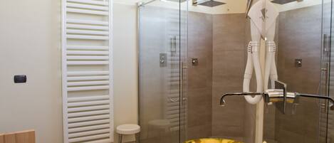 A modern bathroom with a glass-enclosed shower, a white towel rack, and two golden sinks.
