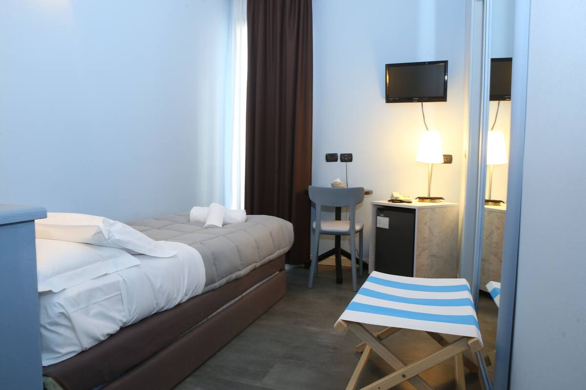 A hotel room with a bed, a desk, a chair, a TV, and a small table with a striped tablecloth.