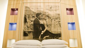 Un dormitorio con una cama grande, un cuadro colgado en la pared de una pareja y dos apliques.