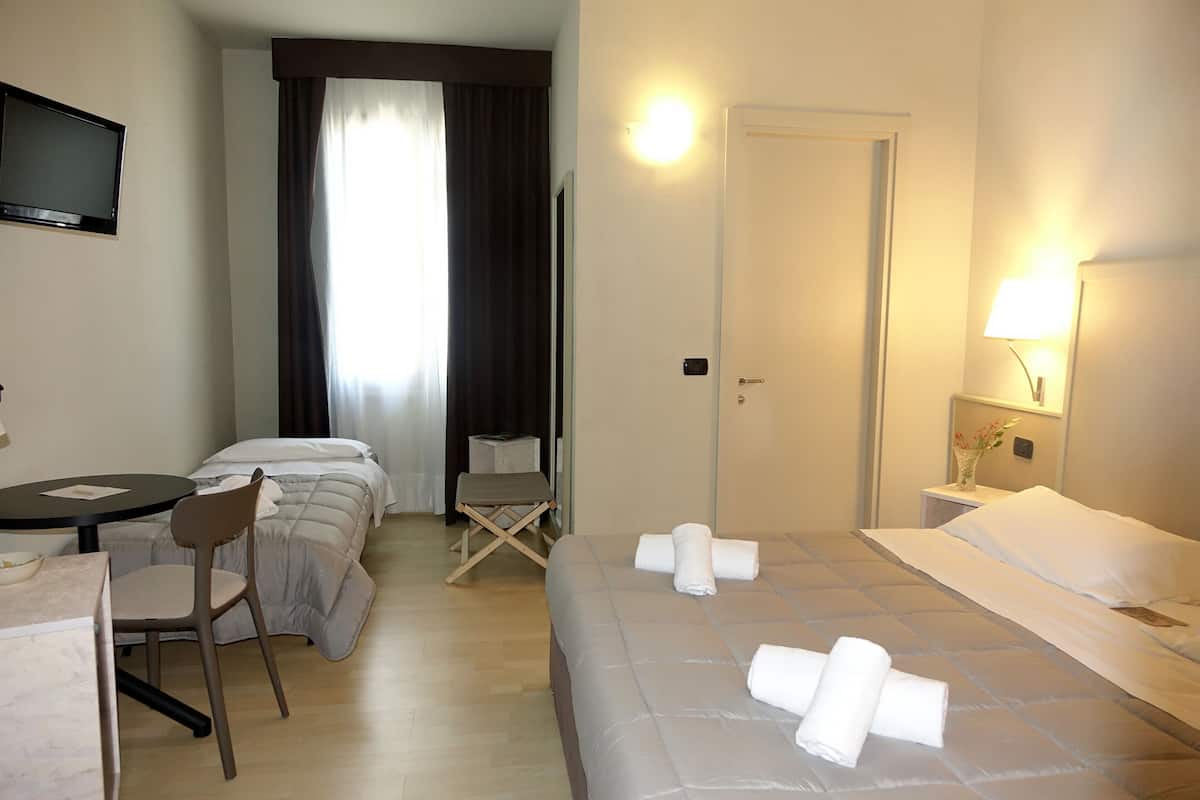 A hotel room with a bed, a desk, a chair, a television, and a door.