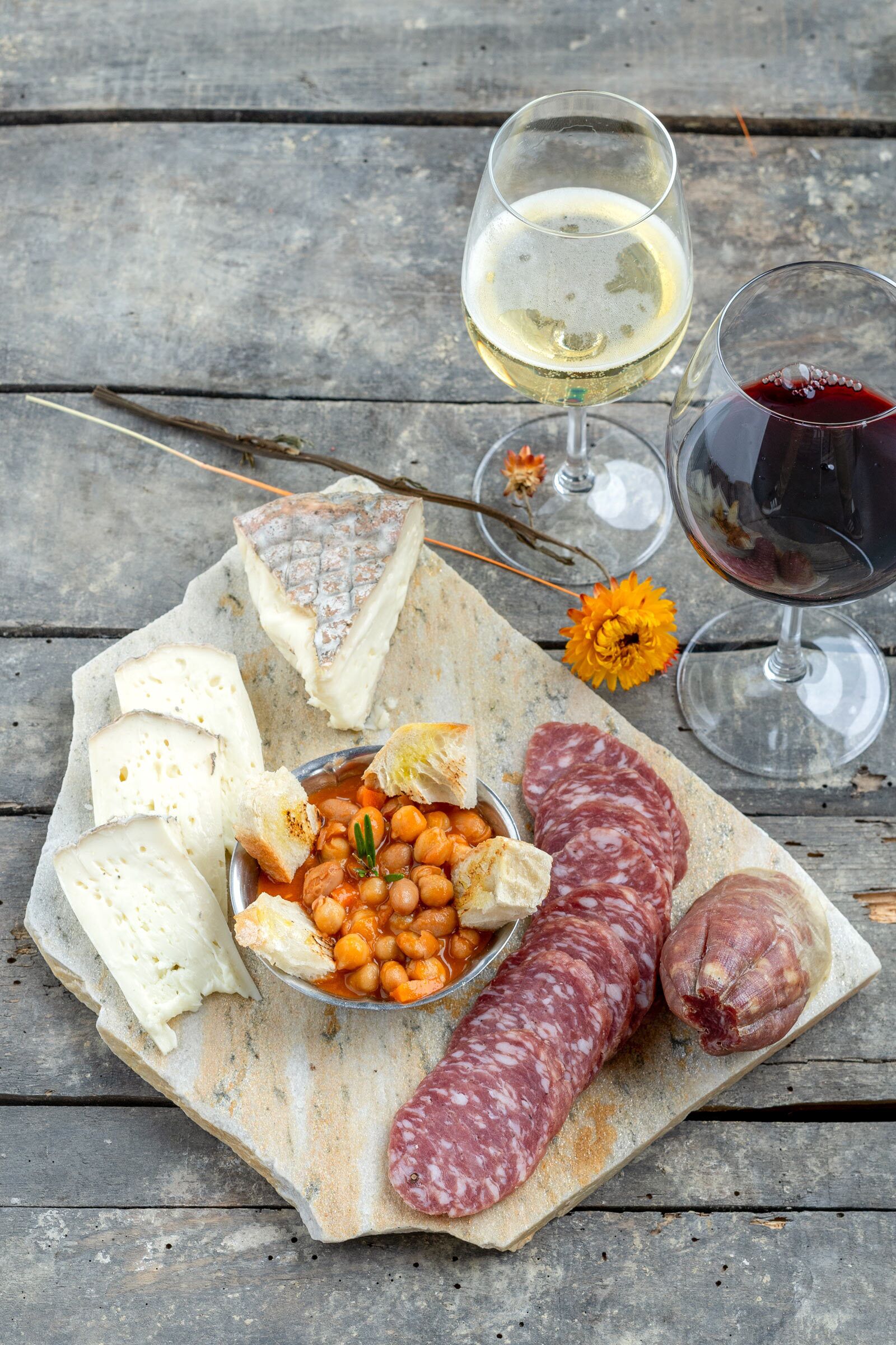 A charcuterie board with various meats, cheeses, and bread, accompanied by two glasses of wine on a wooden surface.