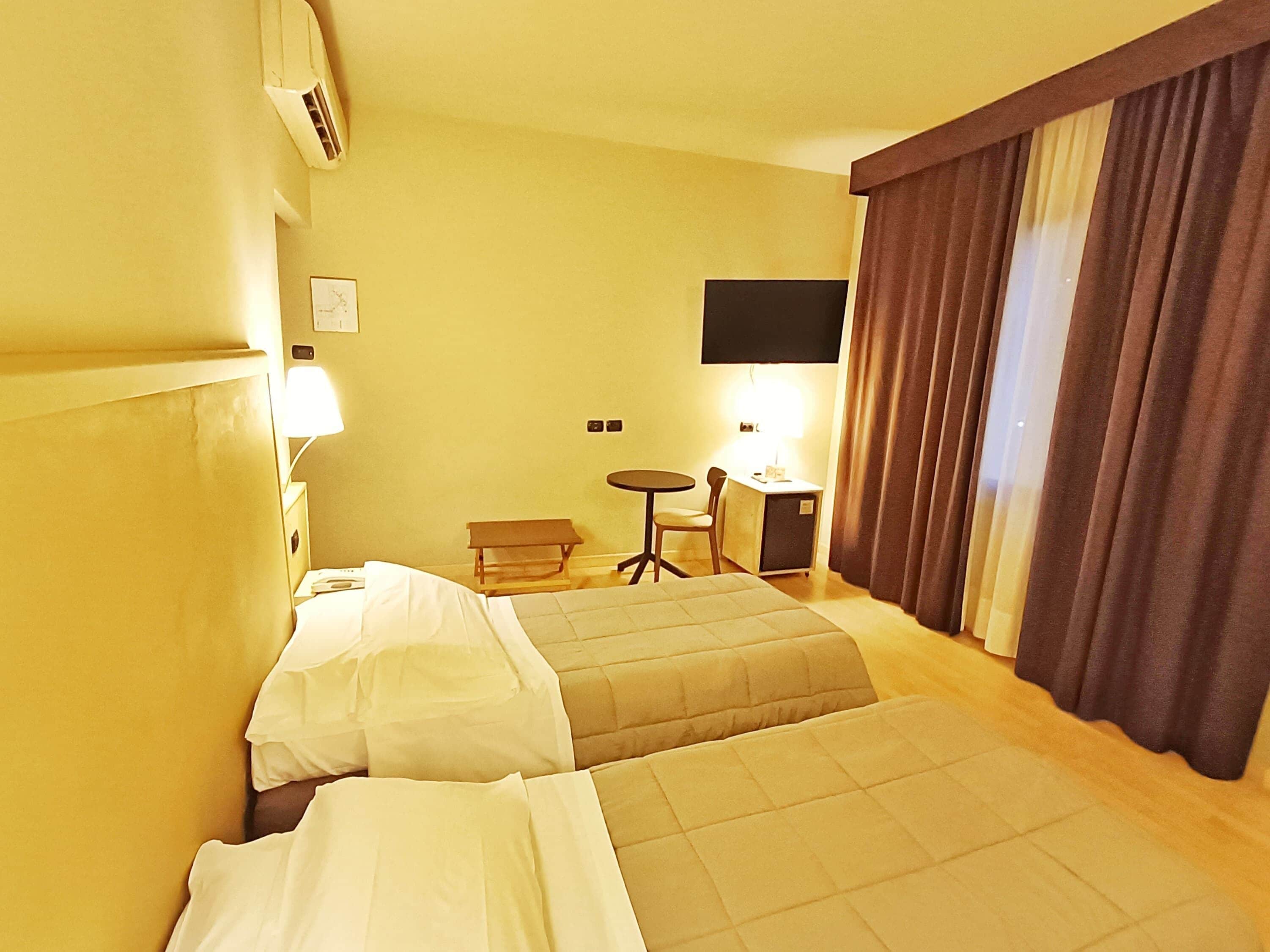 Habitación de hotel con dos camas, un escritorio, una silla, un televisor y una ventana con cortinas.