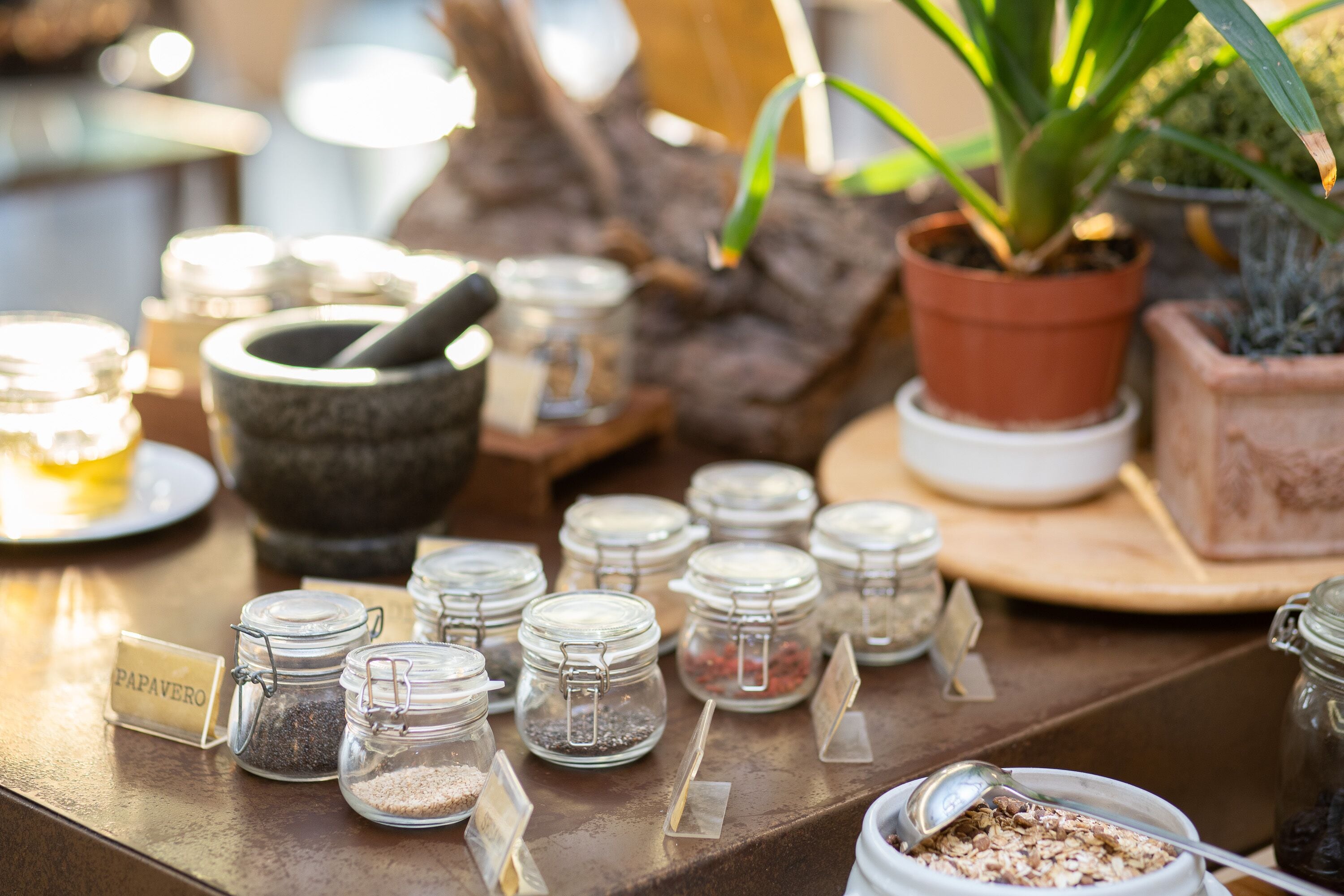 A table with various jars labeled with ingredients like "papavero" and "chia seeds," along with a mortar and pestle.
