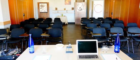 Ett konferensrum med rader av stolar, ett bord med en bärbar dator, en mikrofon och en vattenflaska.