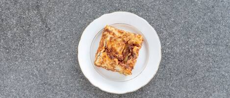 En enda skiva lasagne på en vit tallrik med guldkant, placerad på en grå, strukturerad yta.